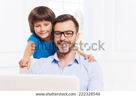 Always ready to help my father. Happy father and son surfing the net at home while little boy pointing laptop monitor and smiling