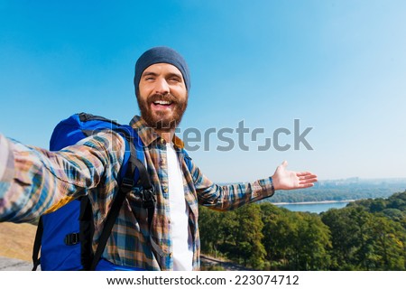 Just look! I am here! Handsome young man carrying backpack and taking a picture of himself and pointing to the view