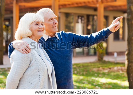 Look over there! Happy senior couple bonding to each other and smiling while man pointing away