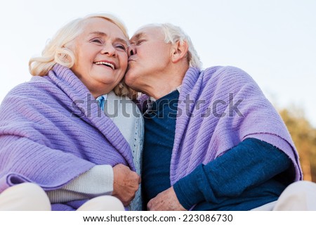 I love you so much! Low angle view of senior man kissing his cheerful wife while being covered with plaid