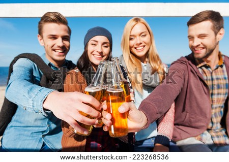 Cheers to friends! Group of young cheerful people cheering with beer and smiling while bonding to each other
