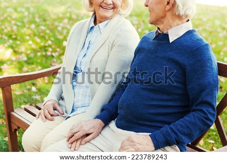 Enjoying their time together. Close-up of happy senior couple holding hands and looking at each other while sitting on the bench in park together
