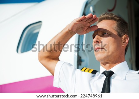 Confident pilot. Confident male pilot in uniform looking at view while standing near the airplane entrance and holding hand upon his eyes