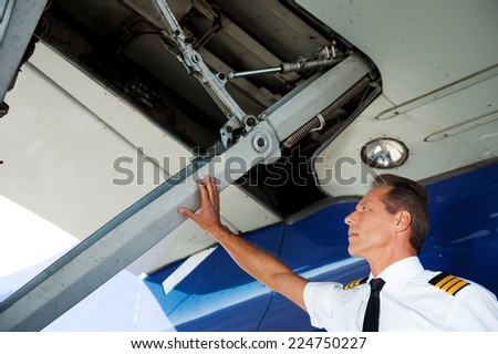Checking the wing. Low angle view of confident male pilot in uniform examining airplane wing