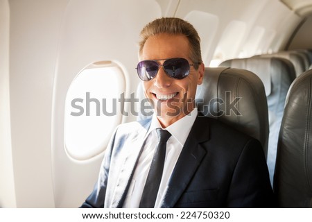 Businessman in airplane. Confident mature businessman sitting at his seat in airplane and smiling