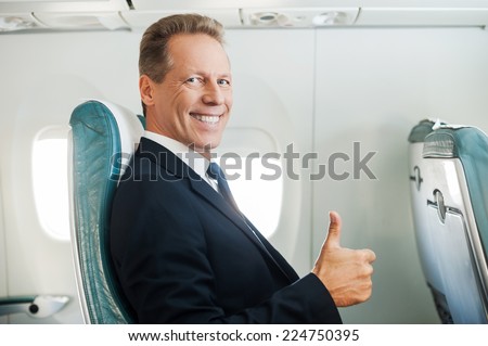 Ready to flight. Confident mature businessman sitting at his seat in airplane and smiling