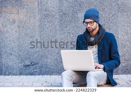 Surfing the net outdoors. Handsome young man in smart casual wear working on laptop while sitting outdoors