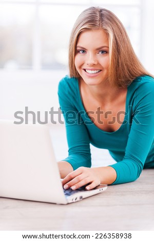 Surfing the net at home. Beautiful young woman working on laptop while lying on the floor at her apartment