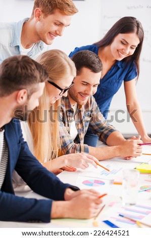 Creative team at work. Side view of five cheerful business people in smart casual wear discussing something while looking at the graphs and charts