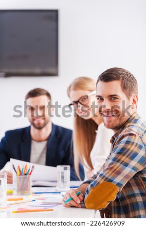 Together we are stronger. Three cheerful business people in smart casual wear sitting together at the table and looking at camera