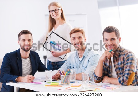 Creative team. Four cheerful business people in smart casual wear sitting together at the table and looking at camera