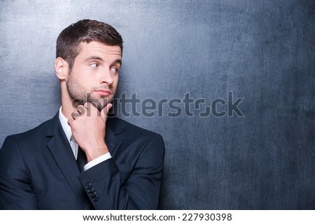 Thoughtful businessman. Handsome young man in shirt and tie holding hand on chin while standing against blackboard