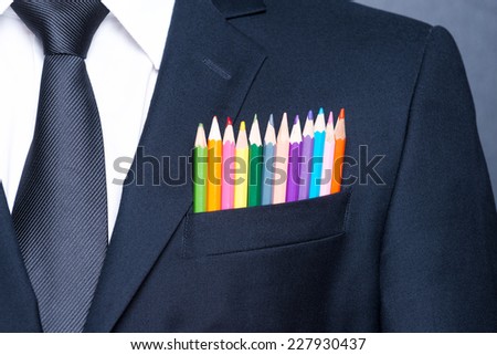 Multicolored businessman.  Close-up of a pocket of businessman with colorful pencils while standing against blackboard