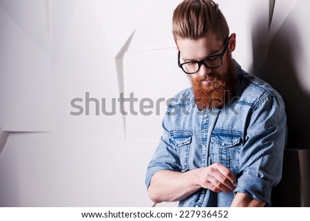 Being attentive the small details. Handsome young bearded man wearing glasses and rolling up sleeves
