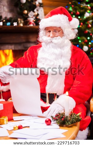 Checking his Christmas list. Concentrated Santa Claus sitting at his chair and reading a letter with envelopes laying on the table