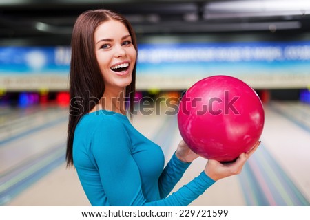 My lucky ball. Beautiful young women holding a bowling ball while standing against bowling alleys