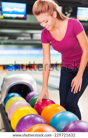 I choose my favorite color. Cheerful young women choosing bowling ball and smiling while standing against bowling alleys