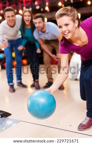 Come on! Beautiful young women throwing  a bowling ball while three people cheering
