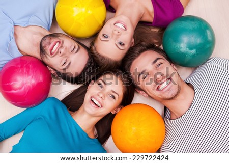 Friendship is always winning in our games. Cheerful friends lying down and near their bowling balls and looking at camera
