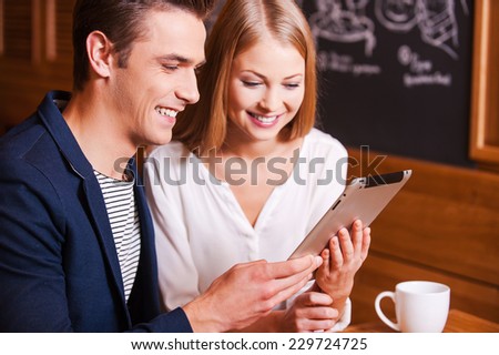 Surfing the net together. Beautiful young couple looking at the digital tablet and smiling while sitting in cafe together