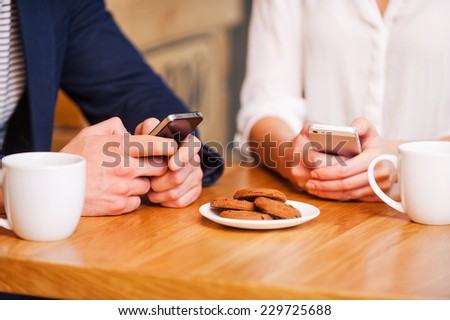 Digital age couple. Close-up of couple texting on their mobile phones while sitting together in cafe