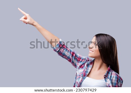 What is on top? Smiling young woman pointing away while standing against grey background