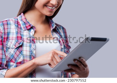 Surfing the net. Close-up of young women working on digital tablet and smiling while standing against grey background