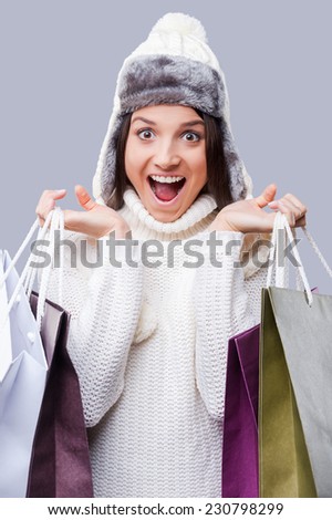 Time for gifts. Happy young women wearing warm winter clothing and holding packages with purchases while standing against grey background