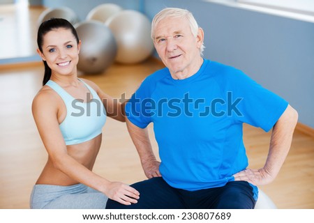 On the road to full recovery. Confident female physical therapist looking at camera and smiling while sitting close to cheerful senior man