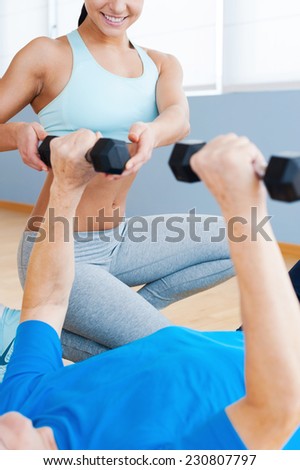 Supporting the all way to recovery. Cropped image of cheerful female personal coach supporting senior man in weight exercises
