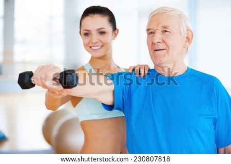 You are doing well! Cheerful female physical therapist helping senior man with fitness in health club