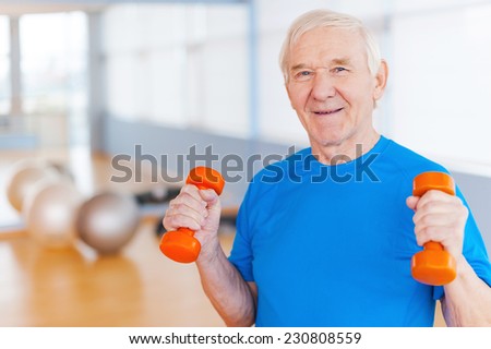 On the road to recovery. Happy senior man exercising with dumbbells and smiling while standing indoors