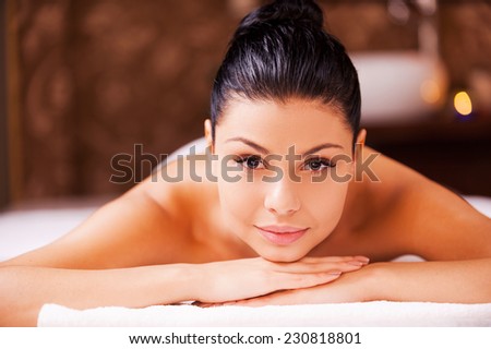 SPA woman. Front view of beautiful young shirtless woman lying on massage table and looking at camera