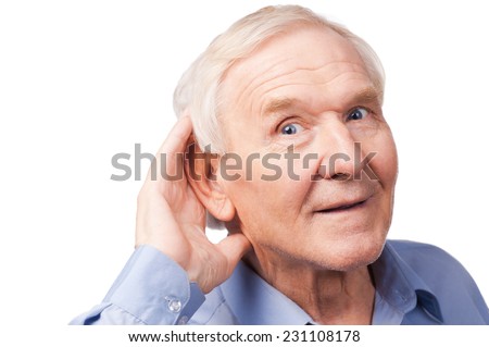 What did you say? Handsome senior man holding hand near his ear and smiling while standing against white background