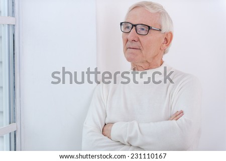 Day dreaming. Thoughtful senior man keeping arms crossed and looking away while leaning at the wall