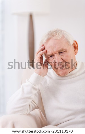 Felling lonely. Frustrated senior man touching his head while sitting in chair
