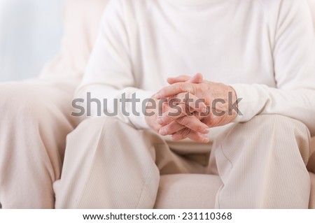 Hands of senior man. Close-up of senior man holding fingers crossed on his hands while sitting in chair