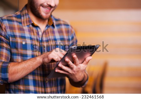 Man surfing the net. Handsome young man working on digital tablet and smiling while standing indoors
