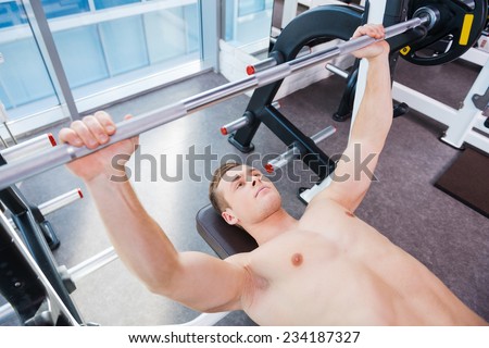 Workout on bench press. Top view of confident young muscular man working out on bench press