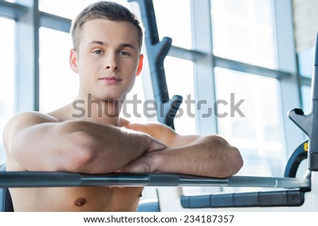 Relaxing after workout. Handsome young muscular man keeping arms crossed and looking at camera while sitting at the bench press