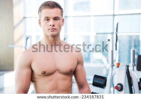 Strength and masculinity. Confident young muscular man looking at camera while standing in gym