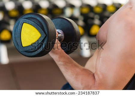 Working at his perfect biceps. Close-up of muscular man working at his biceps while exercising with dumbbells in gym