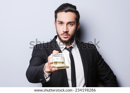 Come to work and get your first salary. Close-up of young man in formalwear stretching out money while standing against grey background