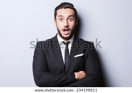 That is unbelievable! Surprised young man in formalwear keeping mouth open and looking at camera while standing against grey background