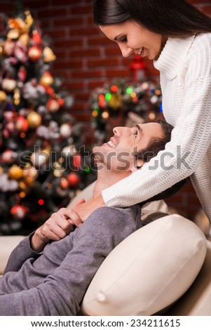 Love is in the air. Side view of beautiful young loving couple bonding to each other and smiling with Christmas Tree in the background