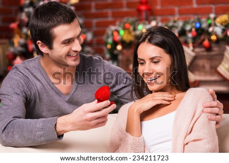 Will you marry me? Handsome young man making a proposal while giving an engagement ring to his girlfriend with Christmas Decoration in the background