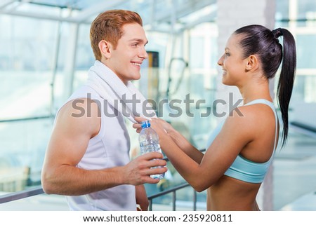 Playful couple in gym. Beautiful young sporty couple talking and smiling while standing in gym