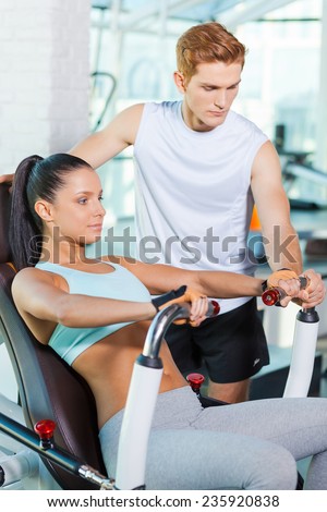 Helping her with exercising. Beautiful young woman working out in gym while confident instructor helping her