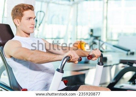 Staying strong and healthy. Handsome young man looking concentrated while working out in gym