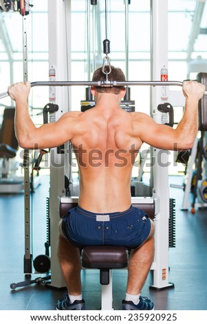 Training his body to perfection. Rear view of young muscular man working out on bench press